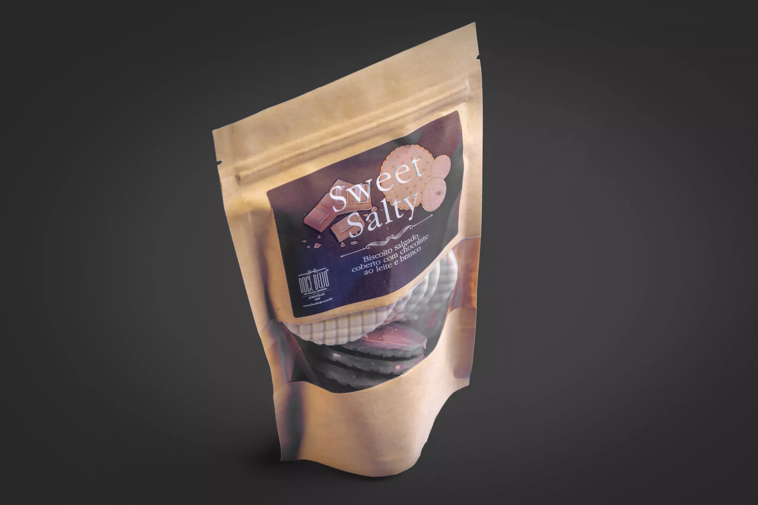 Uma embalagem do tipo "stand-up pouch" do produto "Sweet Salty". O pacote de papel kraft tem uma janela transparente que mostra os biscoitos redondos, nos sabores chocolate ao leite e branco, em seu interior. O rótulo informa que se trata de um "Biscoito salgado coberto com chocolate".